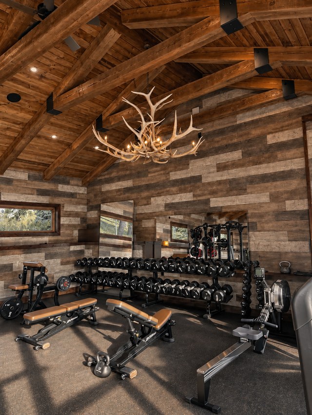 The ranch gym under a timber ceiling with an antler chandelier and training equipment
