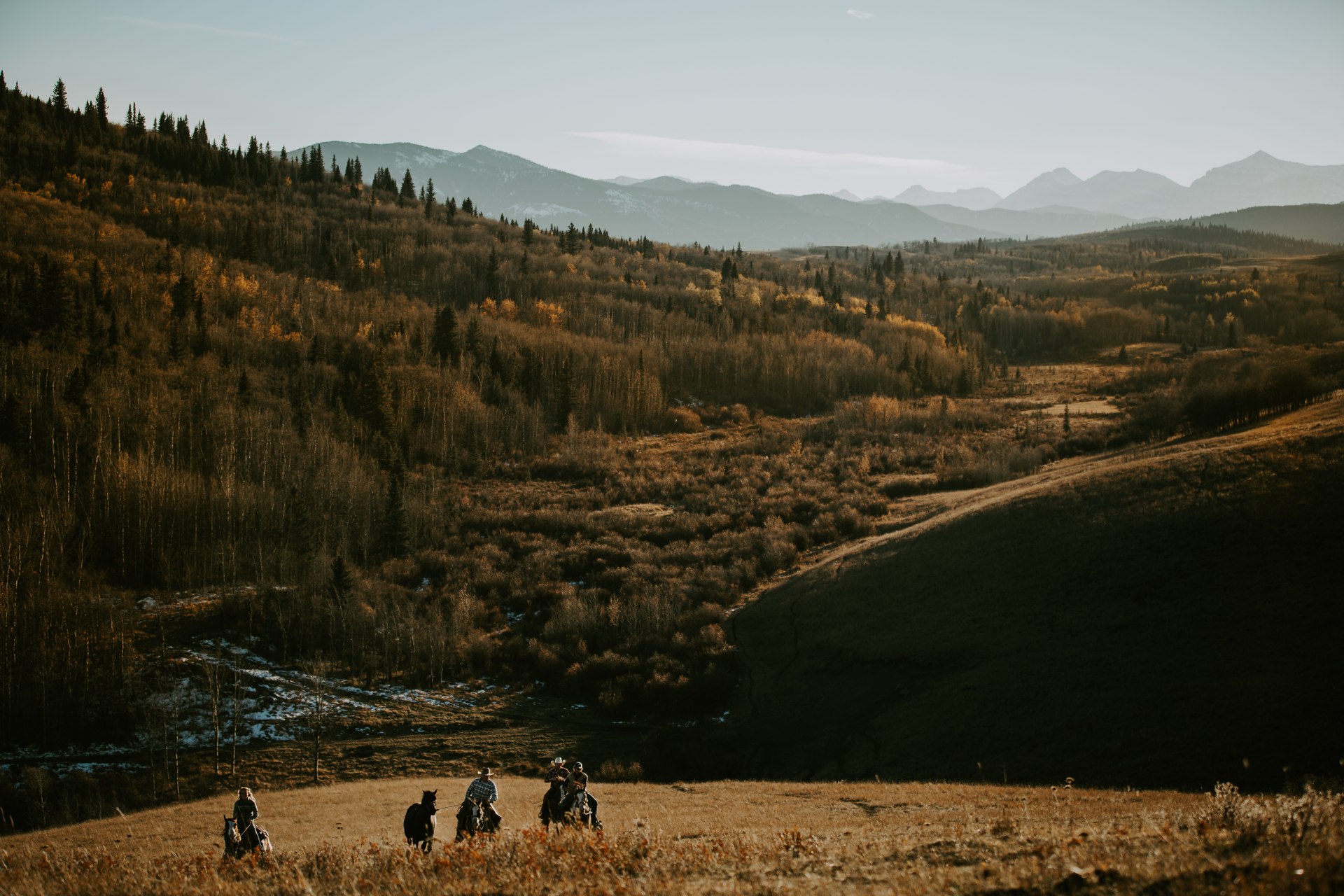 Riders crossing the ranch valley at golden hour, foothills and mountains behind