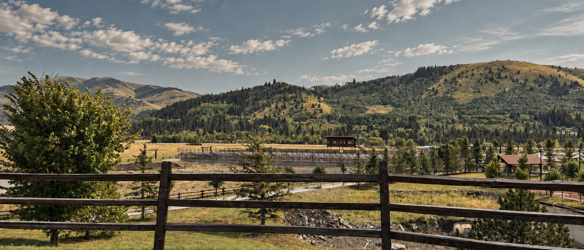 View across the ranch grounds toward the foothills, a fence and tree in the foreground