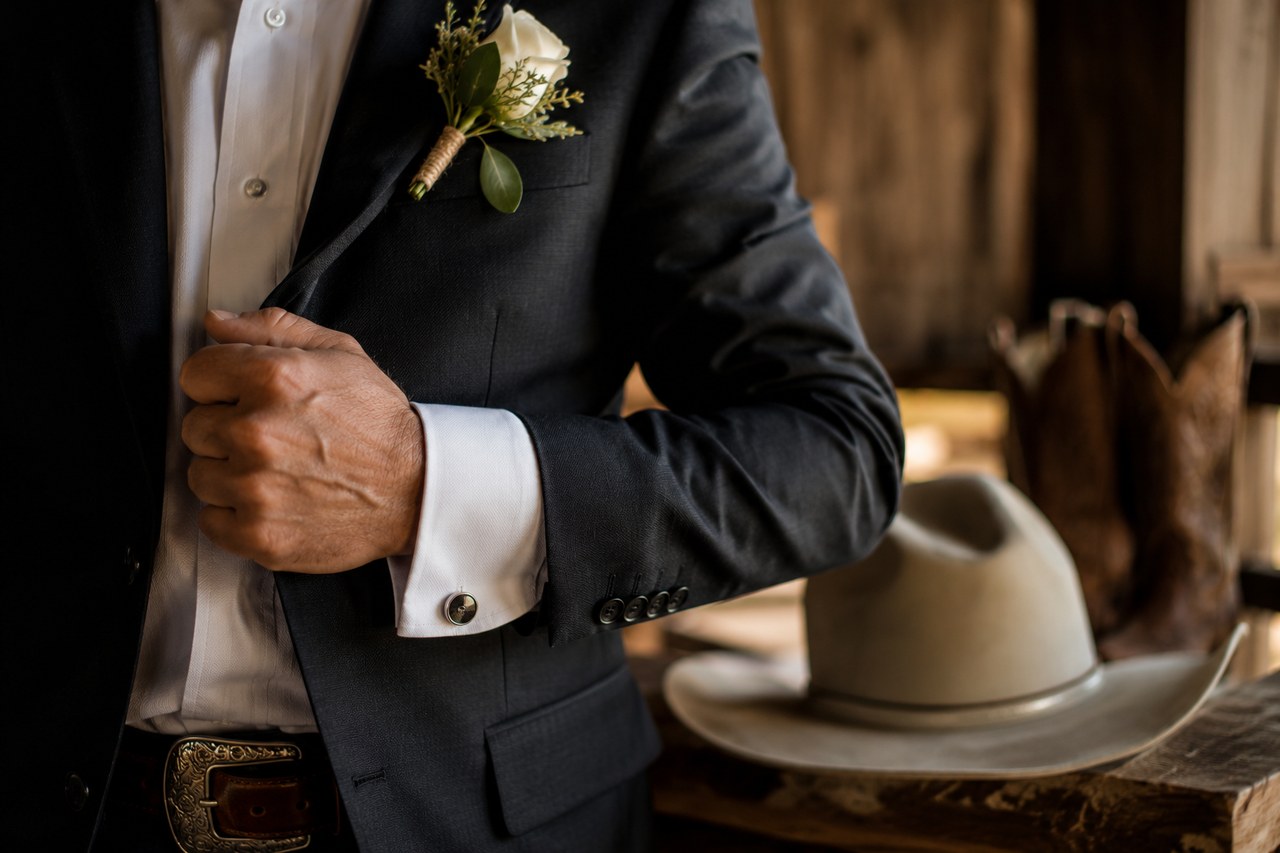 Close-up of the groom's white rose boutonniere and cufflink as he adjusts his jacket