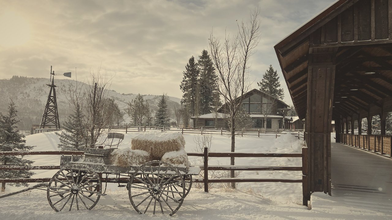 A hay wagon parked under the covered walk in winter, ranch buildings behind